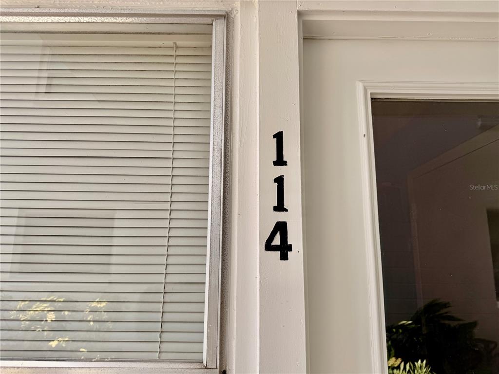 The number 114 is displayed vertically on the white door frame next to a window — 3100 HARTFORD STREET N UNIT 114, ST PETERSBURG, FL