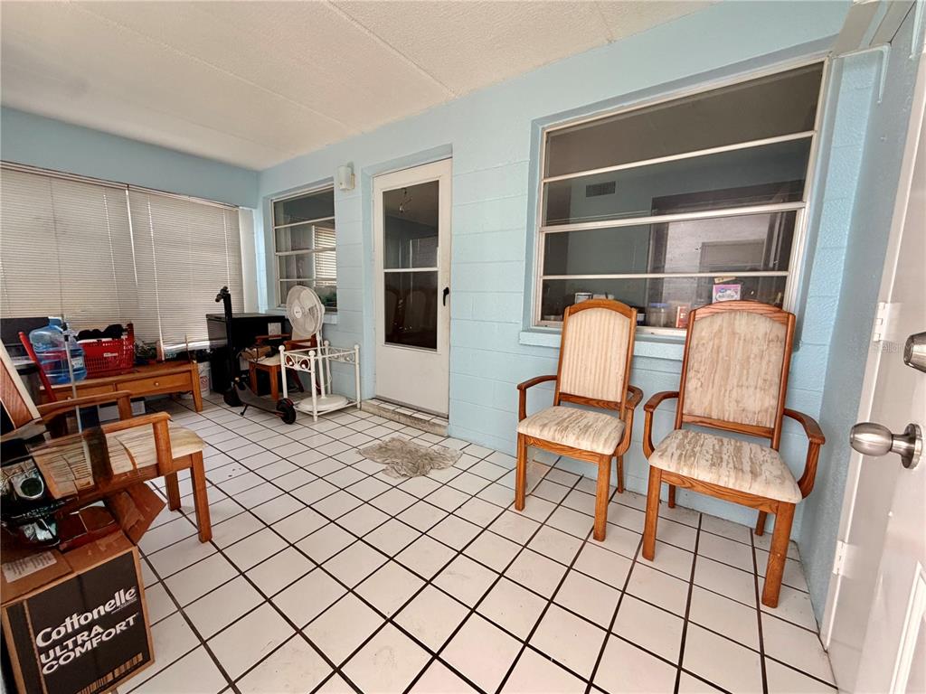 A sunroom with light blue walls, white tiled floors, and two wooden armchairs — 3100 HARTFORD STREET N UNIT 114, ST PETERSBURG, FL