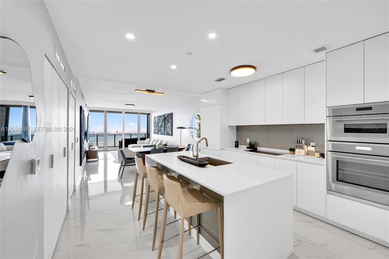 A modern white kitchen features a central island with bar stools and marble flooring — 700 NE 24th St # 5306, Miami FL 33137, MIAMI, FL
