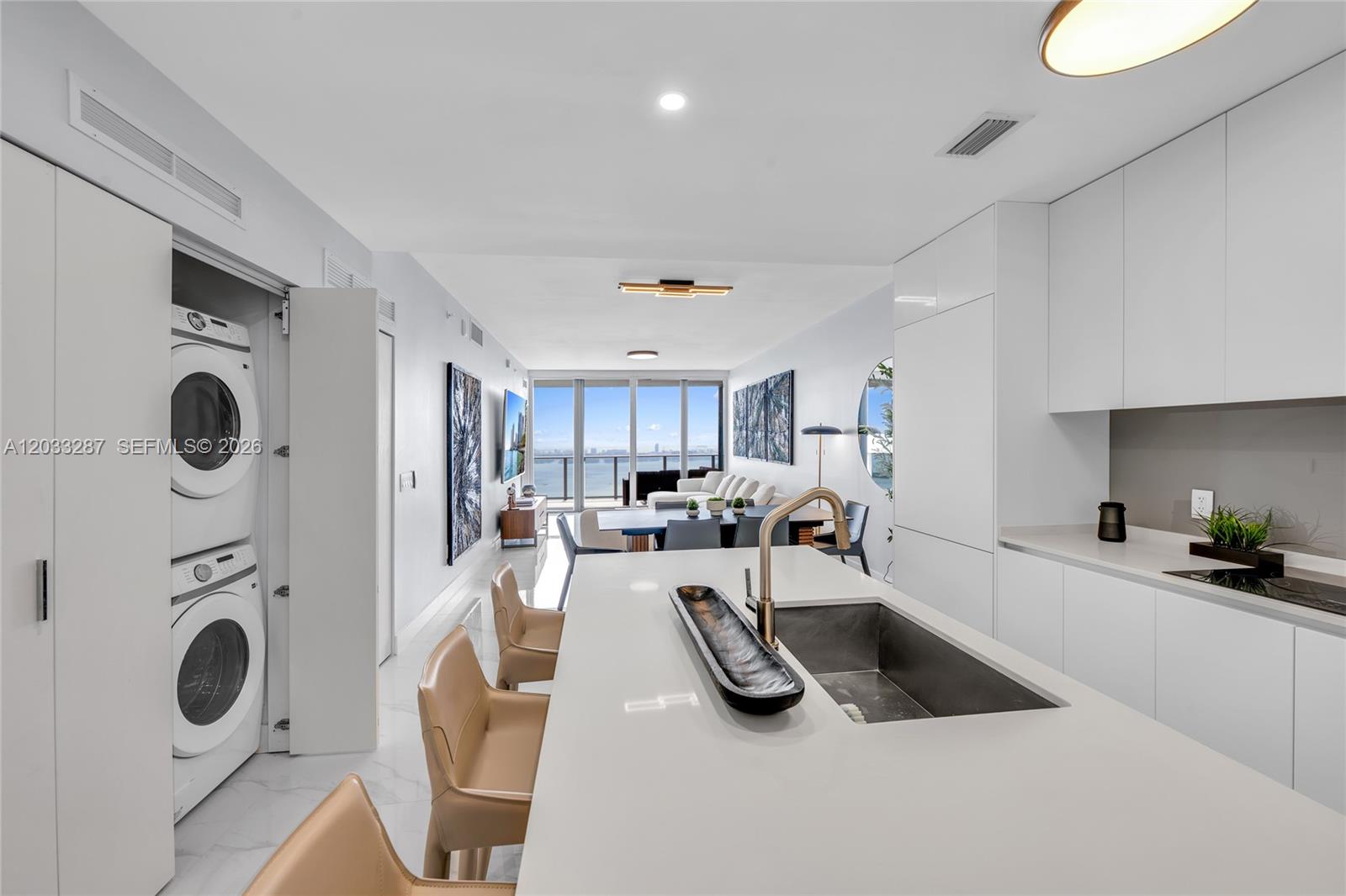 A modern kitchen with a white island and laundry closet overlooks a living area — 700 NE 24th St # 5306, Miami FL 33137, MIAMI, FL