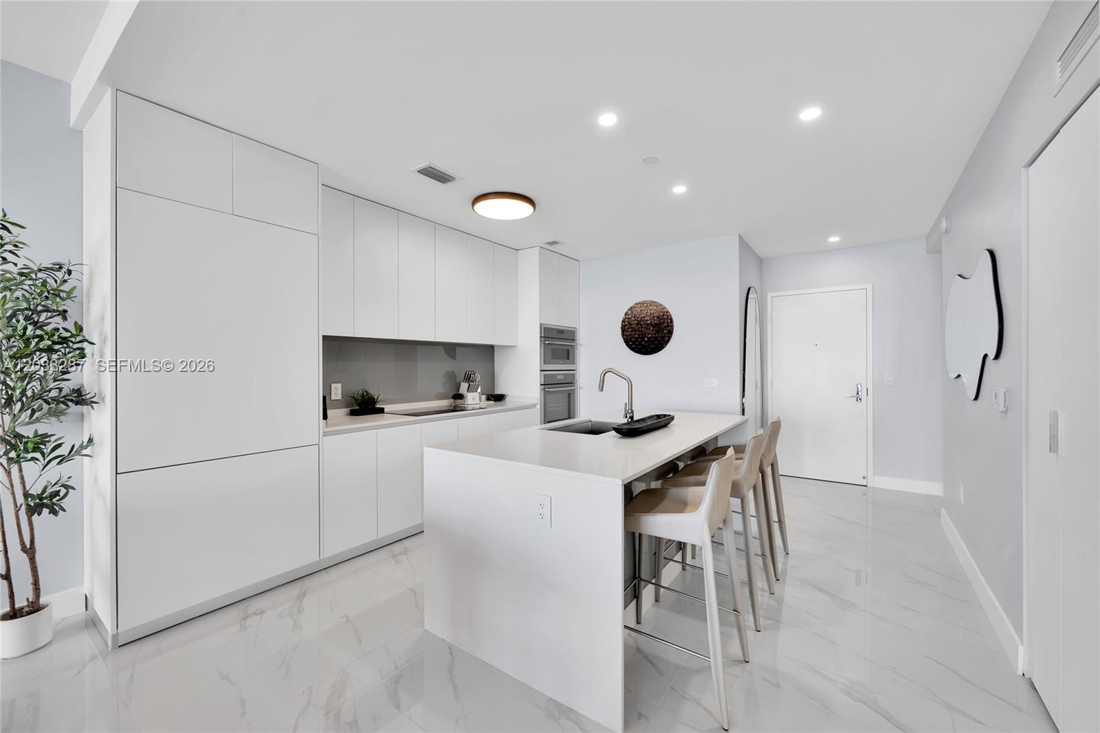 A modern white kitchen features a central island with bar seating and marble-style flooring — 700 NE 24th St # 5306, Miami FL 33137, MIAMI, FL