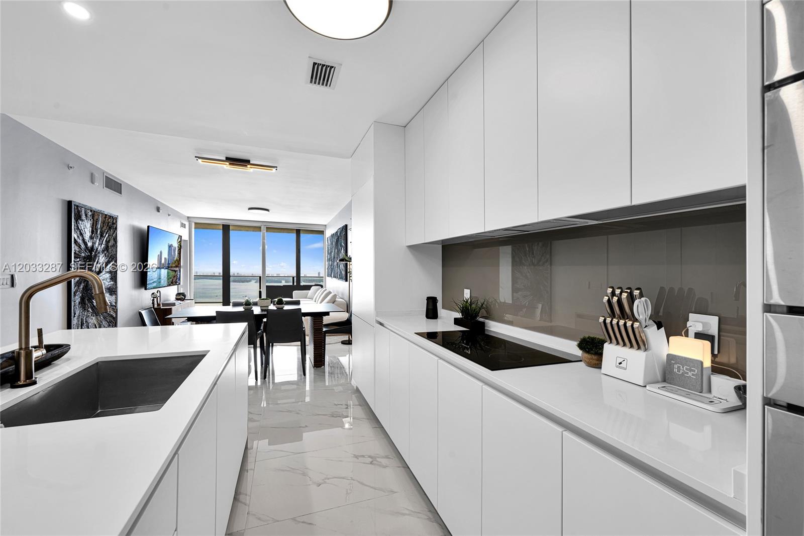 A modern white kitchen features a marble-topped island and a view of the ocean — 700 NE 24th St # 5306, Miami FL 33137, MIAMI, FL