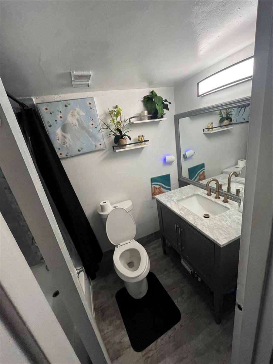 A small bathroom features a gray vanity with a marble countertop, a toilet, and wall shelving — 4364 NW 9th Avenue # 1d, Deerfield Beach FL 33064, DEERFIELD BEACH, FL