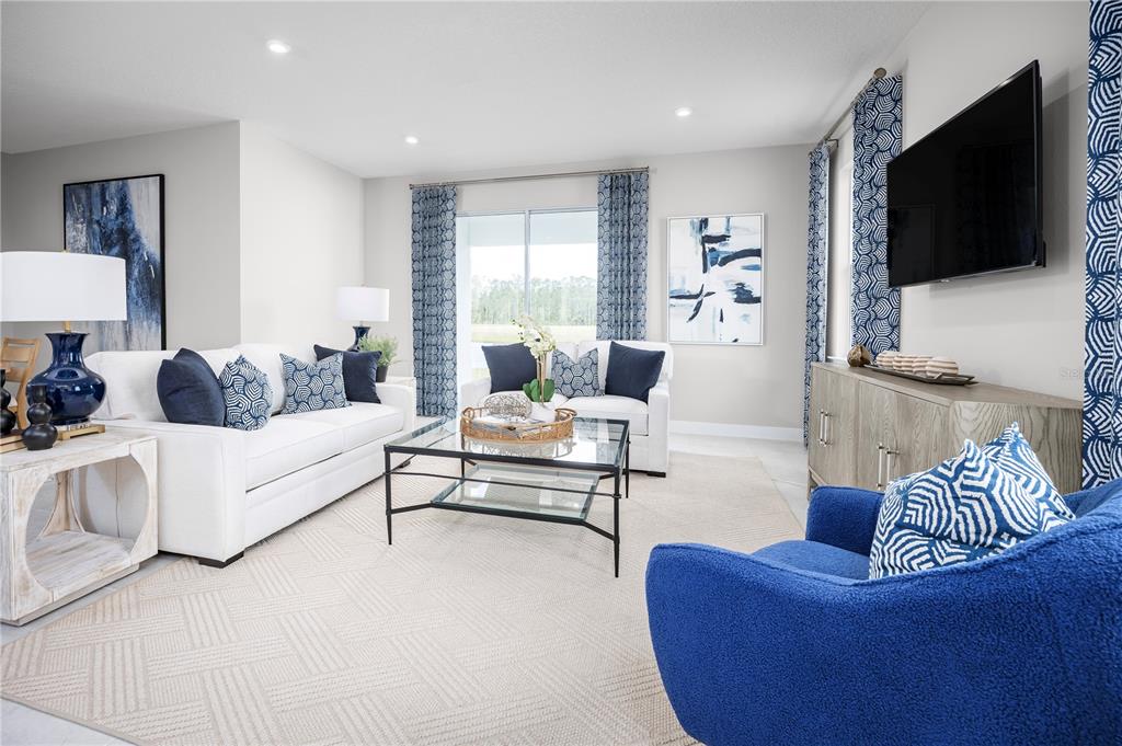 A bright living room features white sofas, a blue armchair, and a glass coffee table — 119 VENETIAN PALMS BOULEVARD, NEW SMYRNA BEACH, FL