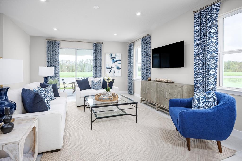 A living room features white sofas, a blue armchair, a glass coffee table, and curtains — 119 VENETIAN PALMS BOULEVARD, NEW SMYRNA BEACH, FL