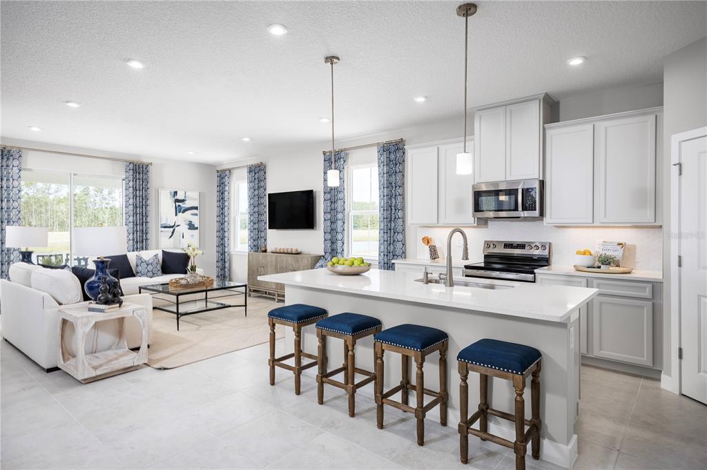 An open-concept kitchen and living area features white cabinetry, a quartz island, and blue accents — 119 VENETIAN PALMS BOULEVARD, NEW SMYRNA BEACH, FL