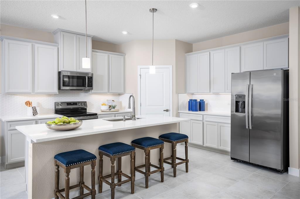 A modern kitchen features white cabinets, stainless steel appliances, a quartz island, and blue stools — 119 VENETIAN PALMS BOULEVARD, NEW SMYRNA BEACH, FL