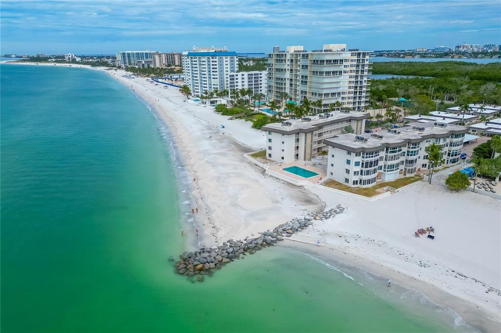 An aerial view of a sandy beach with a rock jetty and beachfront condominium buildings — 1900 BENJAMIN FRANKLIN DRIVE UNIT V12, SARASOTA, FL