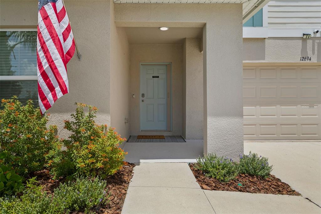 A light blue front door is recessed under a covered entryway next to a garage — 12694 TANNENCREST DRIVE, RIVERVIEW, FL