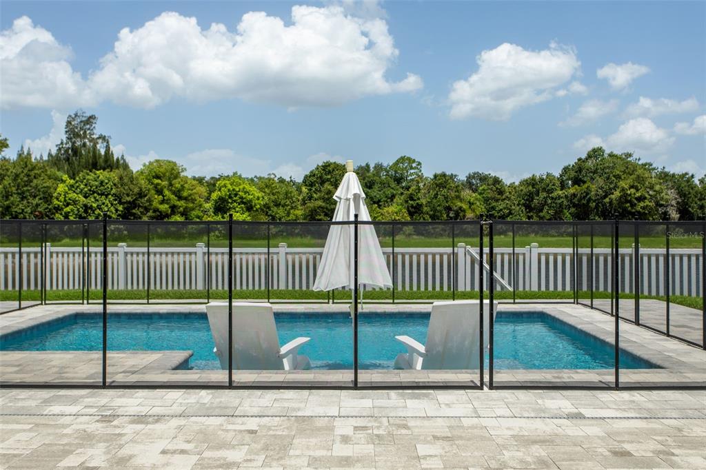 A swimming pool with two lounge chairs and a white umbrella behind a safety fence — 12694 TANNENCREST DRIVE, RIVERVIEW, FL