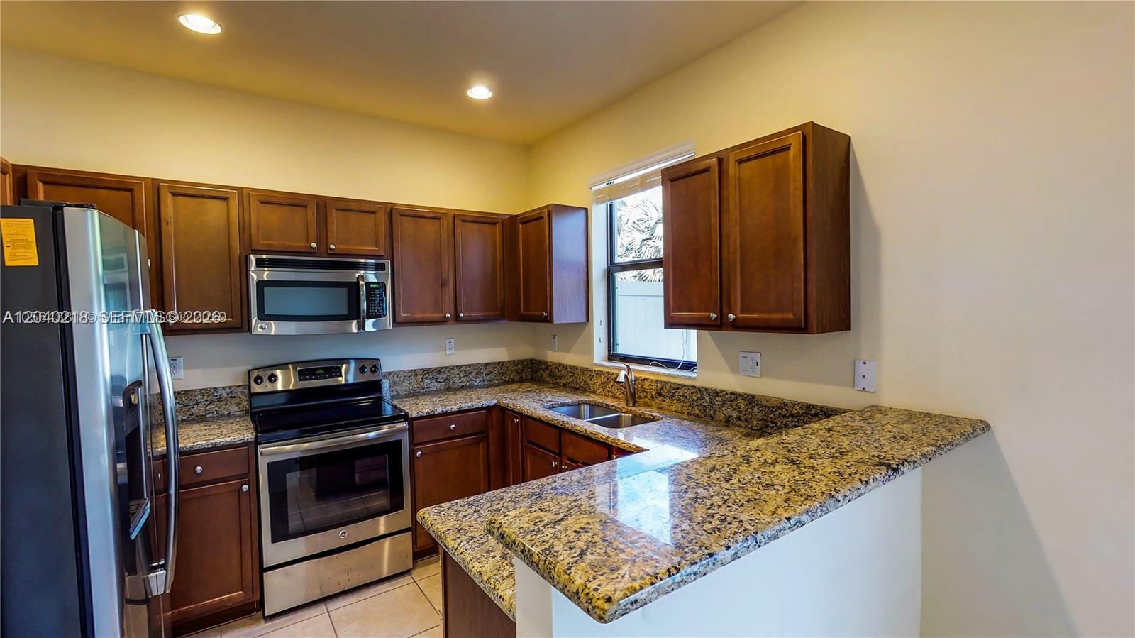 A kitchen features dark wood cabinets, granite countertops, and stainless steel appliances — 9073 W 33rd Ave, Hialeah FL 33018, HIALEAH, FL