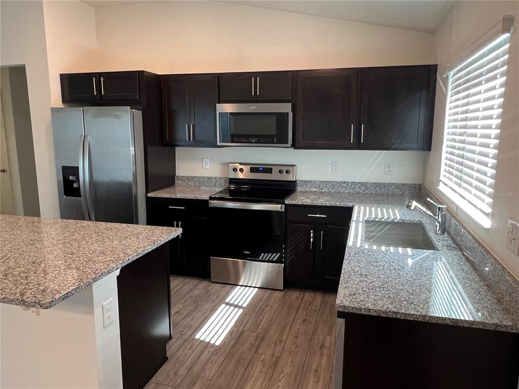 A kitchen features dark wood cabinets, granite countertops, stainless steel appliances, and wood-look flooring — 3838 WHITETAIL COURT, ST CLOUD, FL