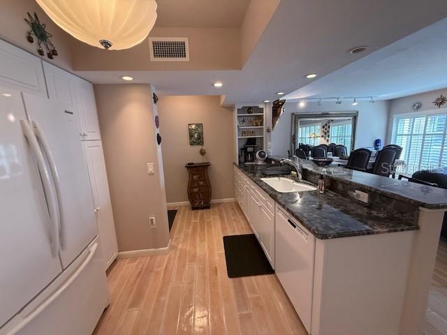 A kitchen features white cabinetry, dark granite countertops, and light wood-look tile flooring — 3806 GULF OF MEXICO DRIVE UNIT C108, LONGBOAT KEY, FL