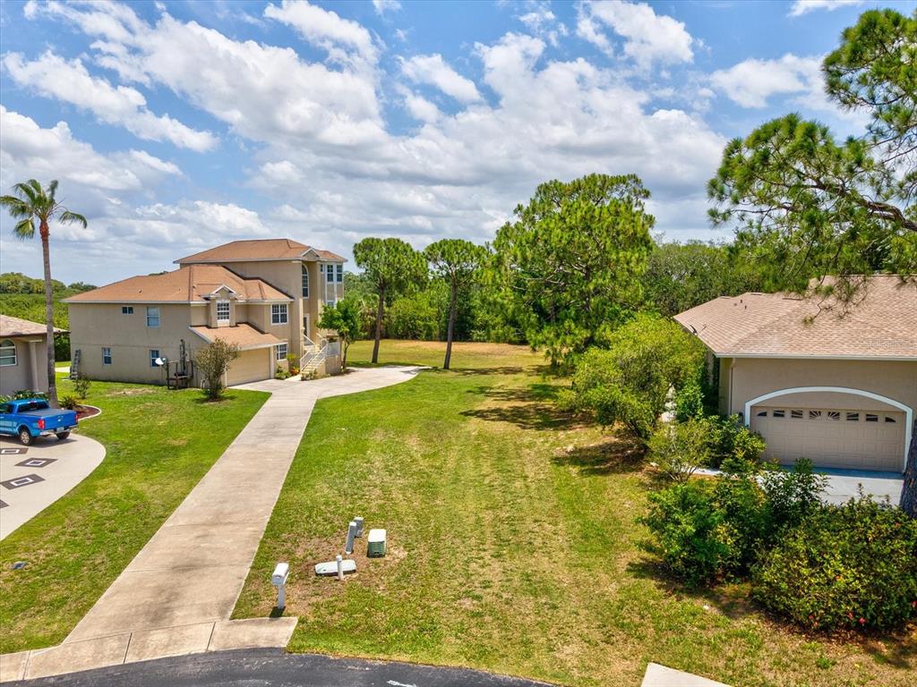 An elevated view shows a grassy lot situated between two suburban houses with driveways — 3046 SHEPPARDS CROOK CT, HOLIDAY, FL