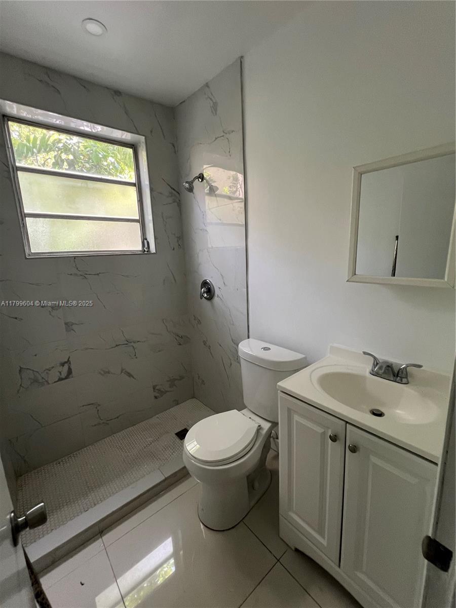 A small bathroom features a walk-in shower with marble-look tile, a toilet, and a vanity — 2345 NW Flagler Ter # 1, Miami FL 33125, MIAMI, FL