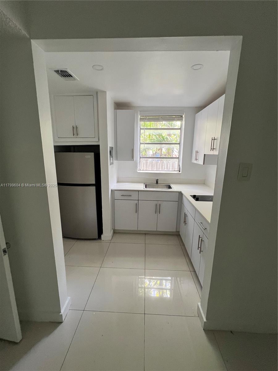 A galley-style kitchen features white cabinets, stainless steel appliances, and light-colored tile flooring — 2345 NW Flagler Ter # 1, Miami FL 33125, MIAMI, FL