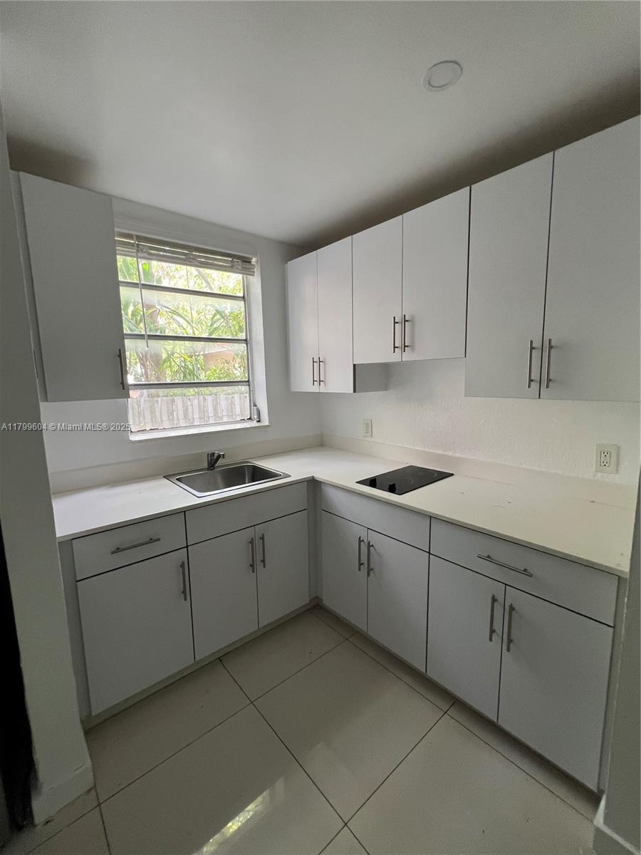 A small kitchen features white cabinets, white countertops, a stainless steel sink, and tile flooring — 2345 NW Flagler Ter # 1, Miami FL 33125, MIAMI, FL