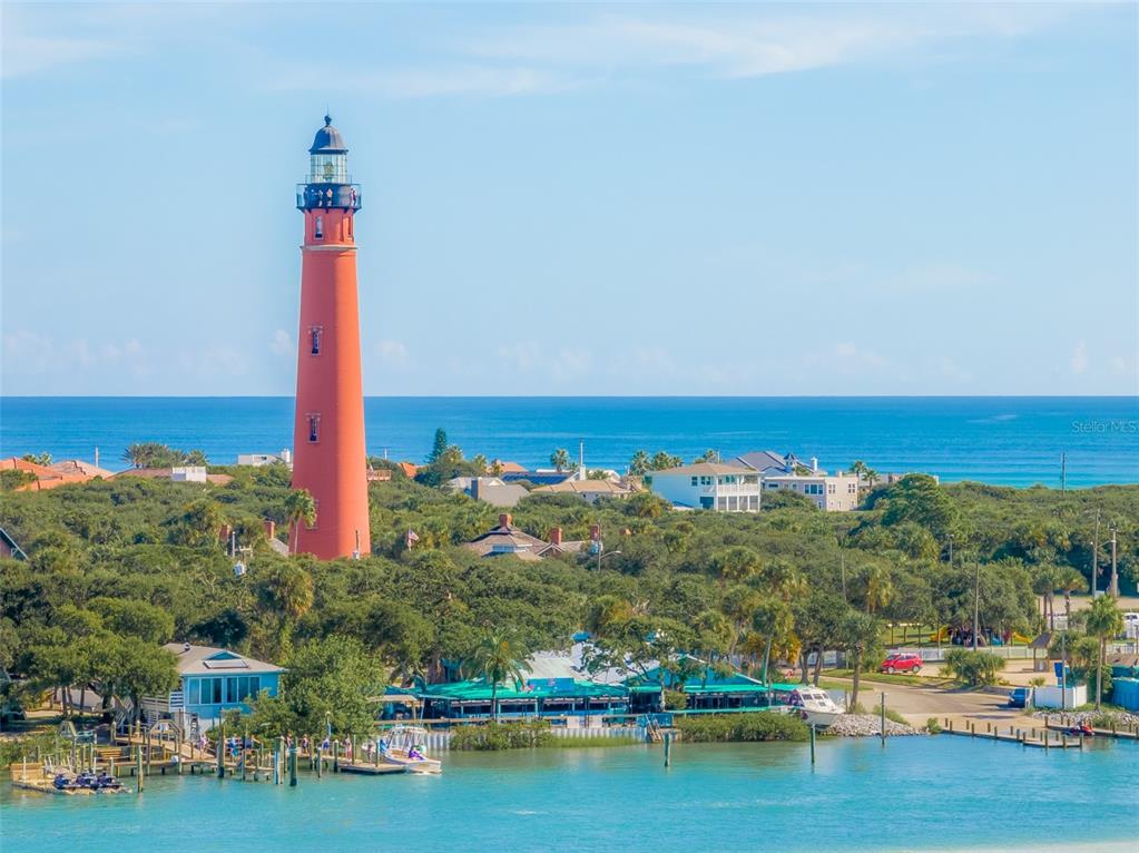 A tall red lighthouse stands near a coastal town with lush trees and blue water — 4861 S ATLANTIC AVENUE, PONCE INLET, FL