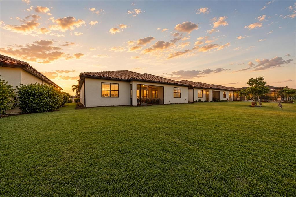 A wide, grassy backyard view of the rear exterior of a single-story stucco house — 538 FIRE BUSH COURT, BRADENTON, FL