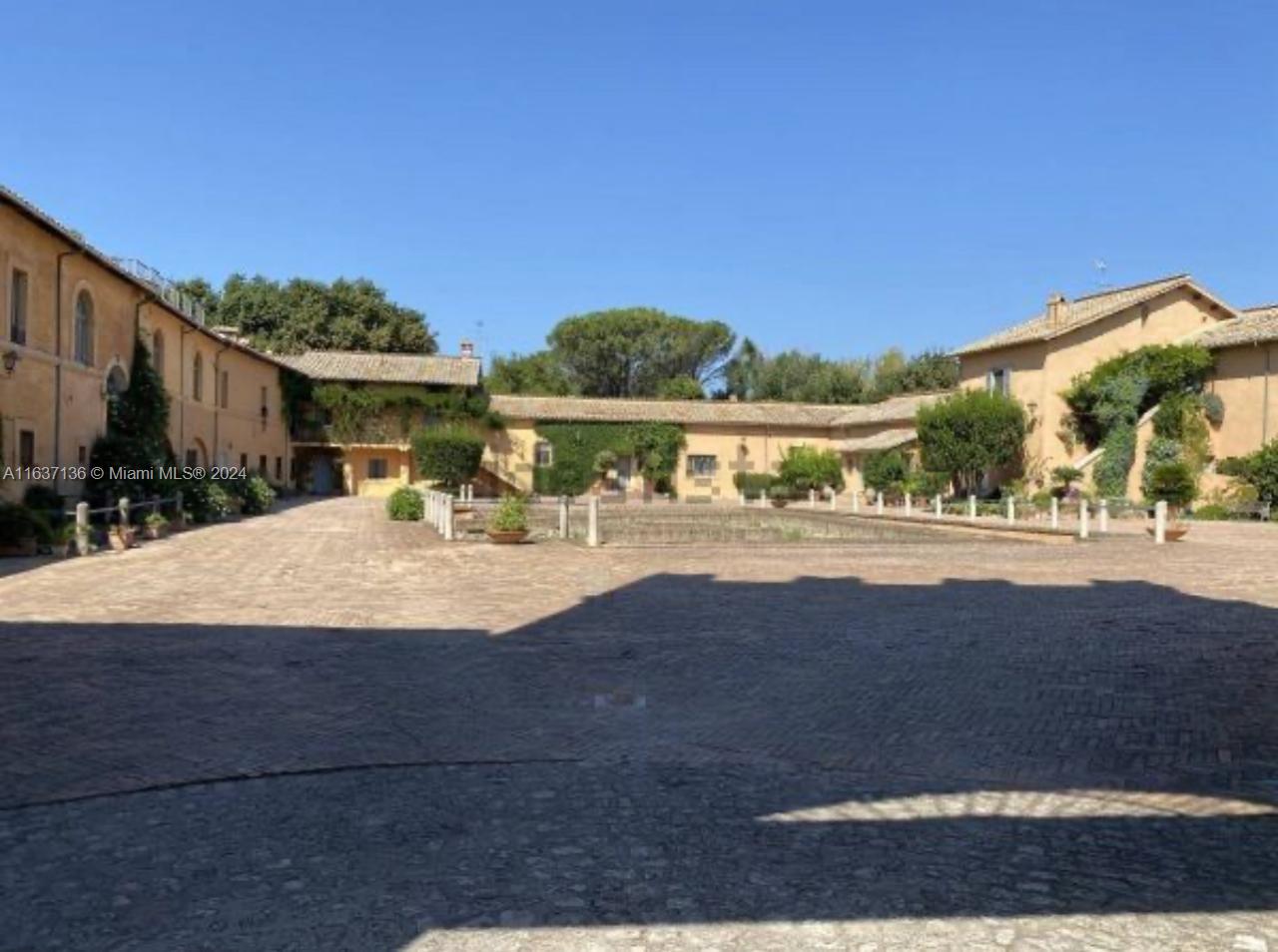 A large, stone-paved courtyard is surrounded by historic, multi-story buildings with tiled roofs — 4 NW Via tiberina, 00100, FL