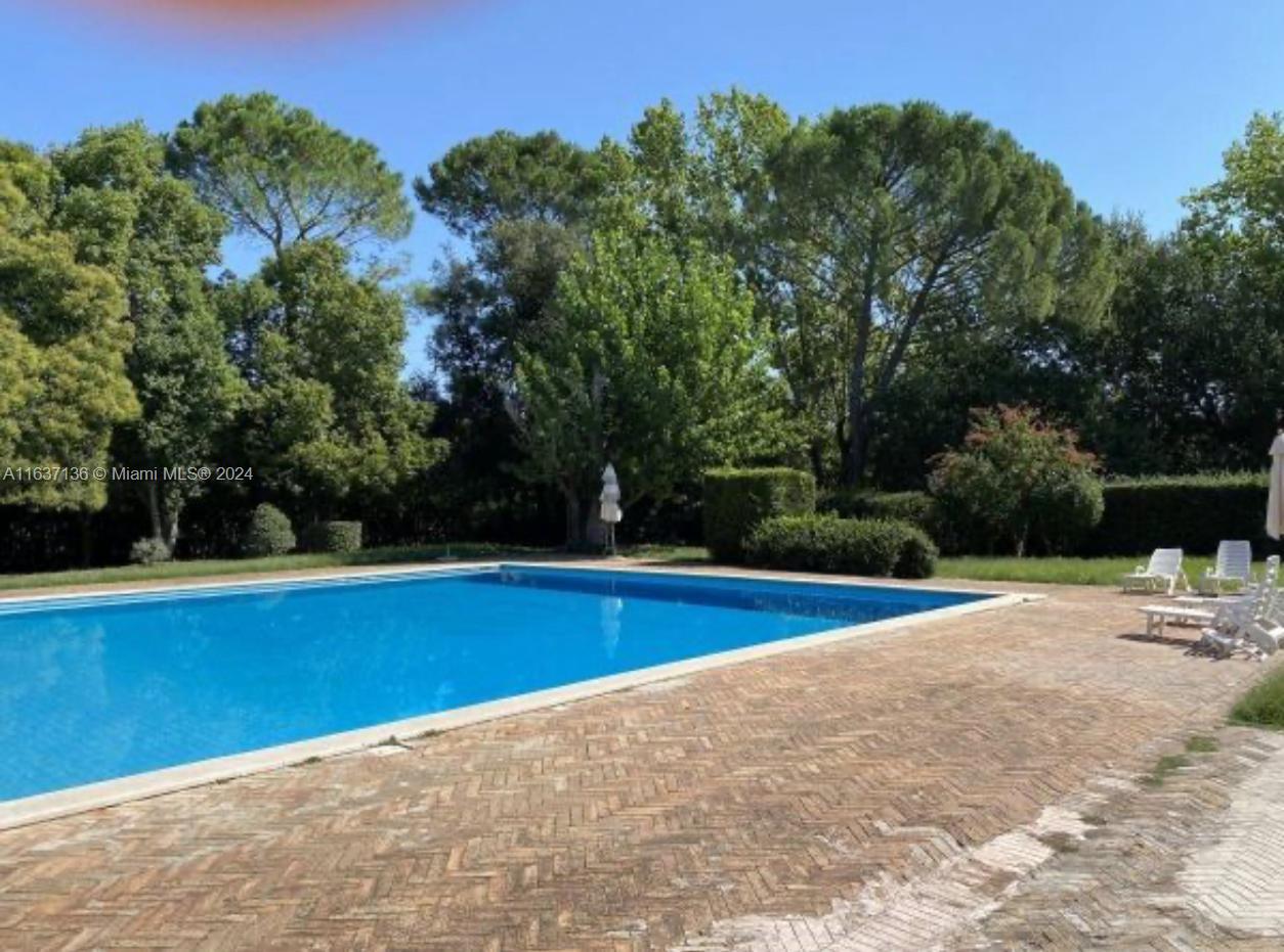 A rectangular swimming pool sits on a brick patio surrounded by trees and lawn — 4 NW Via tiberina, 00100, FL