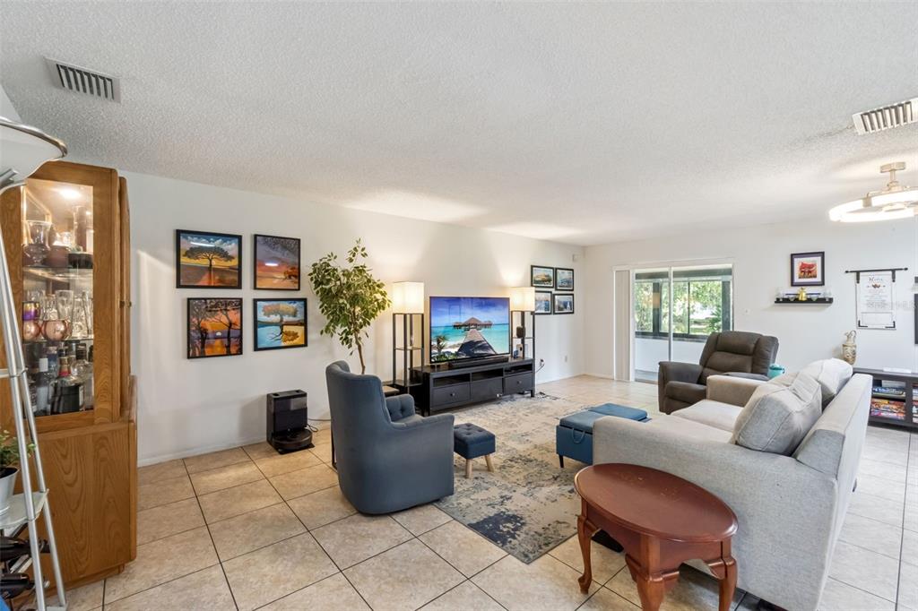 A living room features tile flooring, a grey sofa, a blue armchair, and a television — 10044 GARRISON LANE, ORLANDO, FL