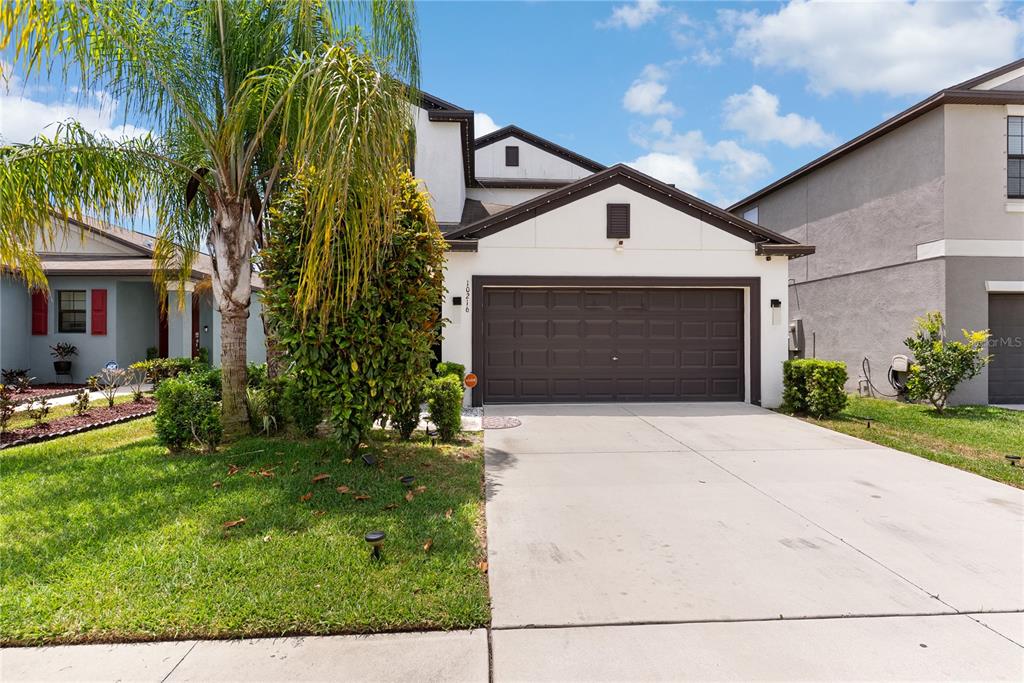 A two-story house with a white stucco facade, a dark garage door, and a palm tree — 10216 CARLOWAY HILLS DRIVE, WIMAUMA, FL