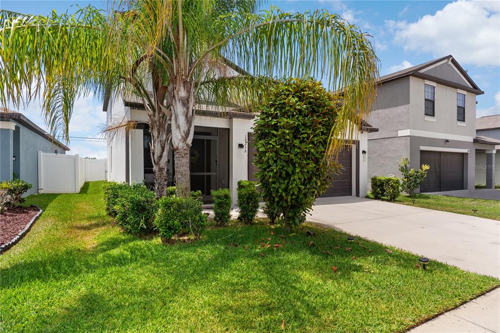 A two-story suburban house features a palm tree, manicured shrubs, and a concrete driveway — 10216 CARLOWAY HILLS DRIVE, WIMAUMA, FL