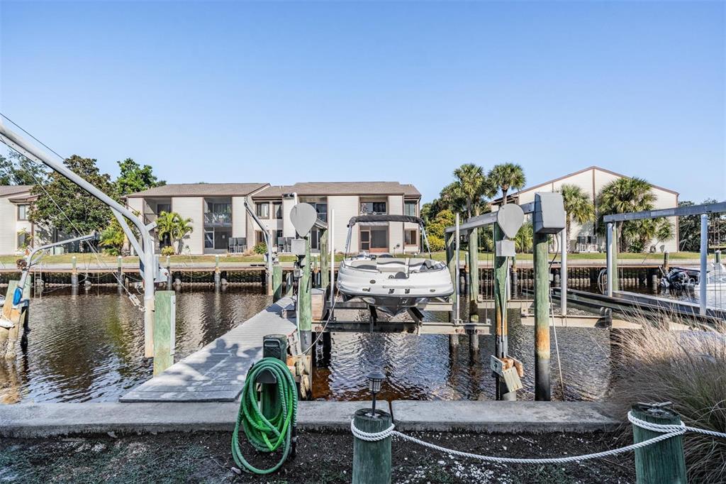 A boat sits on a lift at a wooden dock in front of apartment buildings — 200 MERES BOULEVARD UNIT 16, TARPON SPRINGS, FL