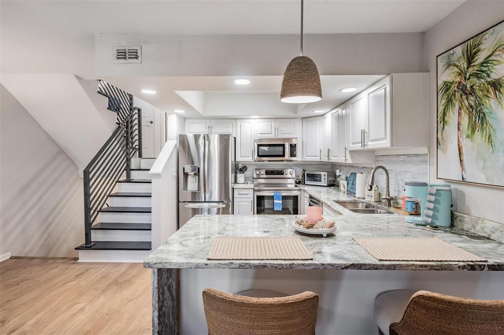 A kitchen features white cabinetry, stainless steel appliances, a granite island, and an adjacent staircase — 200 MERES BOULEVARD UNIT 16, TARPON SPRINGS, FL