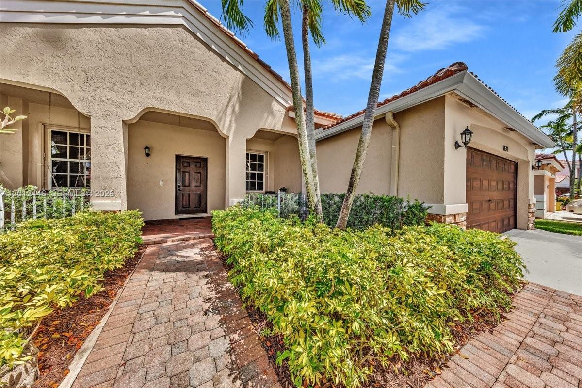 A tan stucco house features a brick walkway, a dark front door, and a garage — 1634 Sandpiper Cir, Weston FL 33327, WESTON, FL