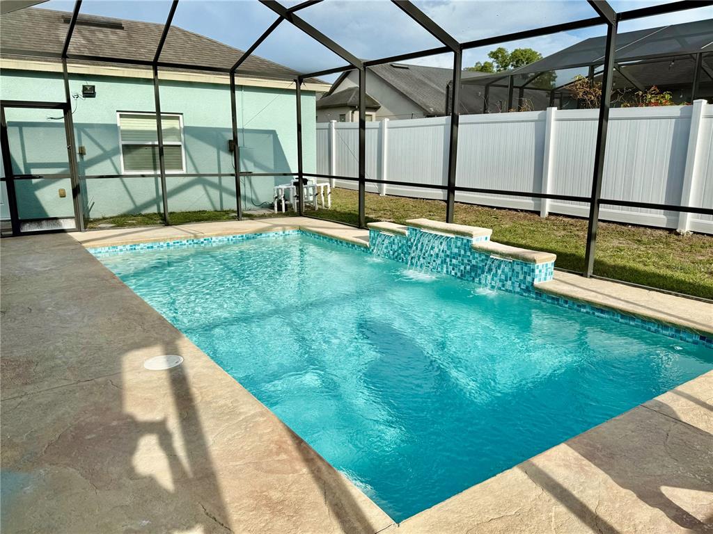 A rectangular swimming pool with a tiled water feature sits inside a screened-in patio enclosure — 1201 LAVENDER JEWEL COURT, PLANT CITY, FL