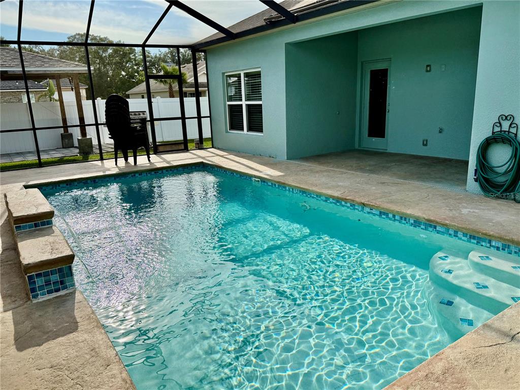 A swimming pool with steps and a tiled bench sits inside a screened-in patio area — 1201 LAVENDER JEWEL COURT, PLANT CITY, FL