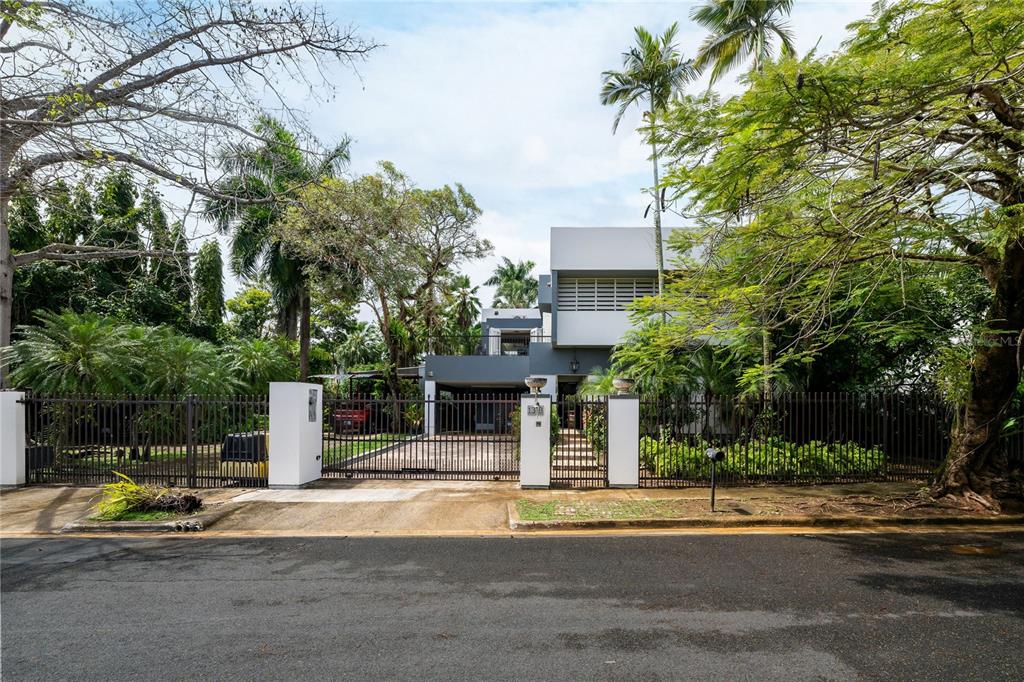 A modern two-story house sits behind a gated driveway surrounded by lush tropical trees — 13 PEDROSA ST. GARDEN HILLS, GUAYNABO, PR