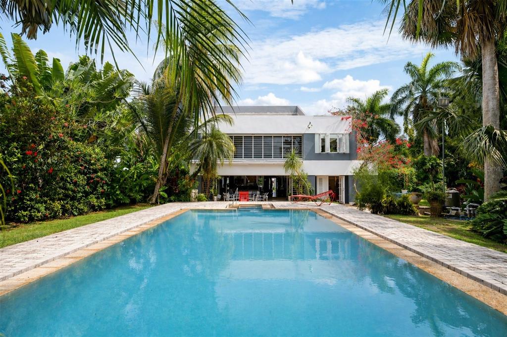 A rectangular swimming pool sits in front of a two-story house surrounded by lush tropical landscaping — 13 PEDROSA ST. GARDEN HILLS, GUAYNABO, PR