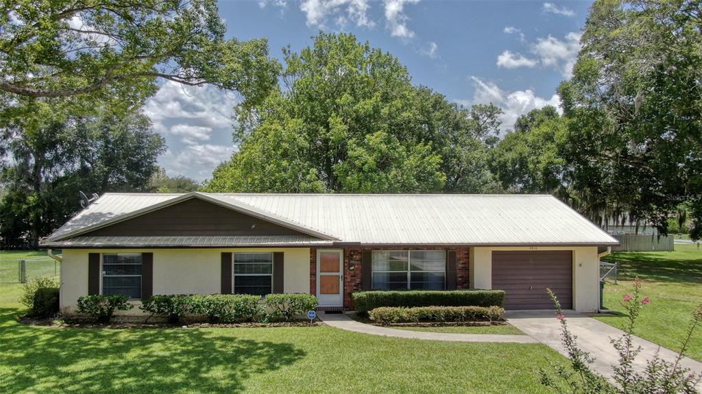 A single-story house with a white metal roof, tan exterior, and an attached garage — 4816 NE 6TH STREET, OCALA, FL