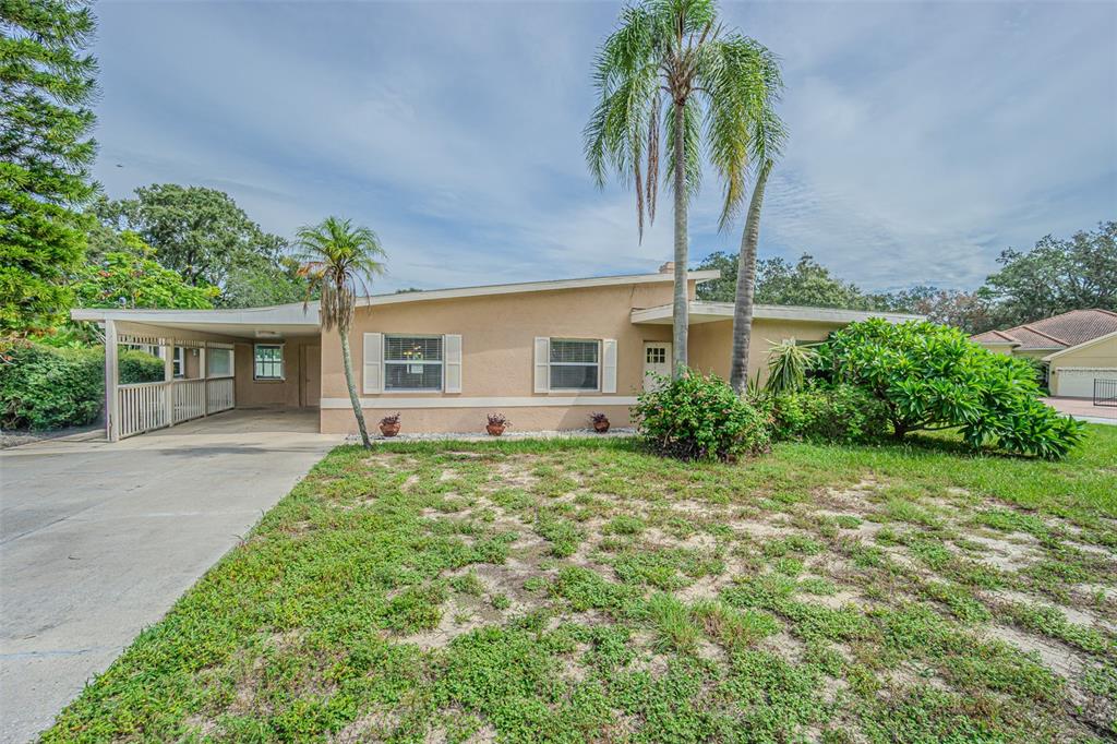 A single-story house with a carport, tan stucco exterior, and palm trees in the yard — 912 RIVERSIDE DRIVE, TARPON SPRINGS, FL