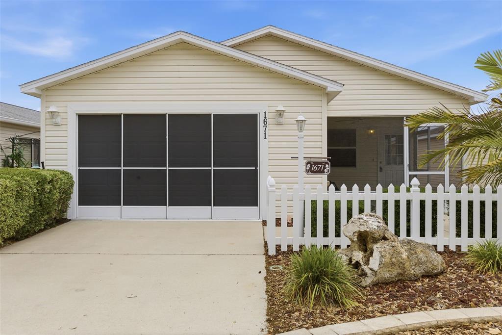 A single-story house with light siding, a screened garage door, and a white picket fence — 1671 OSPREY AVENUE, THE VILLAGES, FL