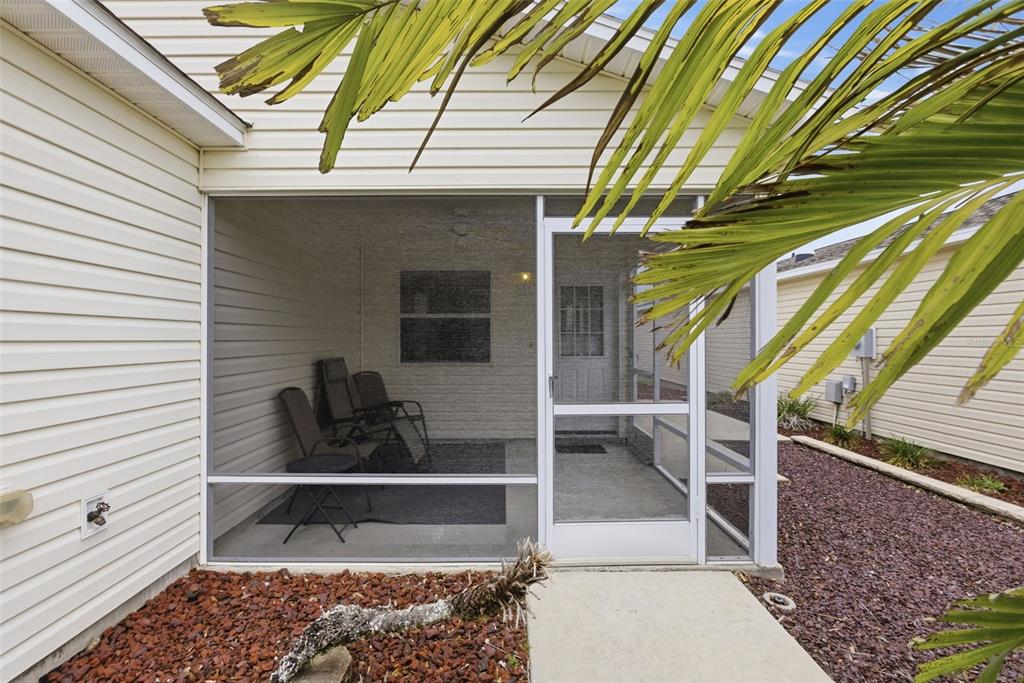 A screened-in porch with chairs and a door sits beside a house with beige siding — 1671 OSPREY AVENUE, THE VILLAGES, FL