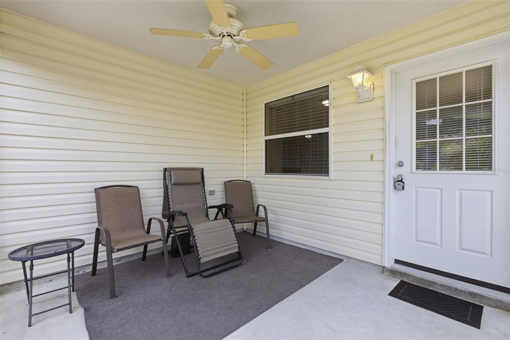 A covered porch with light-colored siding, a ceiling fan, three chairs, and a white door — 1671 OSPREY AVENUE, THE VILLAGES, FL