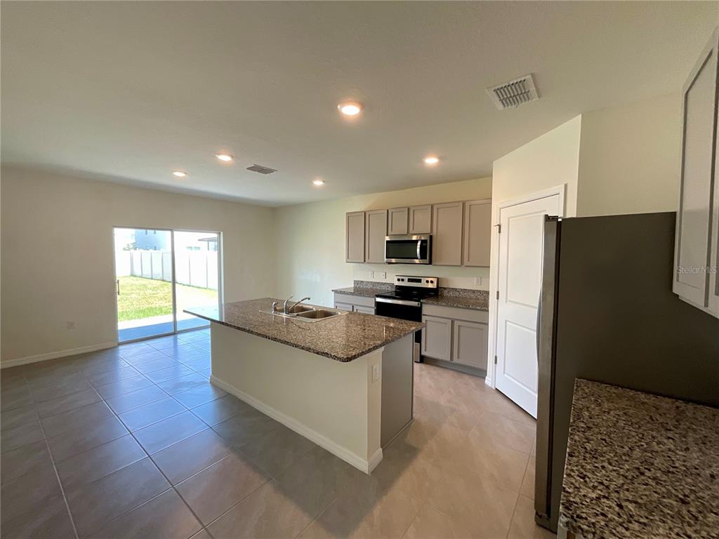A kitchen features a granite-topped island, gray cabinetry, stainless steel appliances, and tile flooring — 33409 FIELD MAPLE LOOP, WESLEY CHAPEL, FL