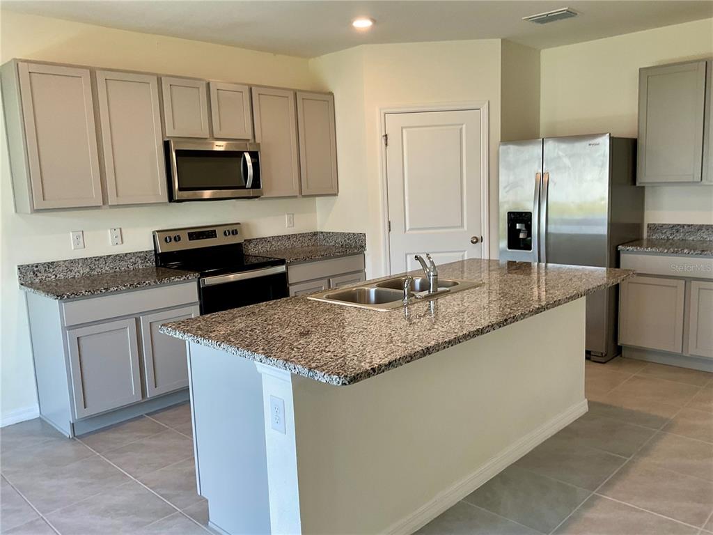 A kitchen features gray cabinets, granite countertops, stainless steel appliances, and a central island — 33409 FIELD MAPLE LOOP, WESLEY CHAPEL, FL