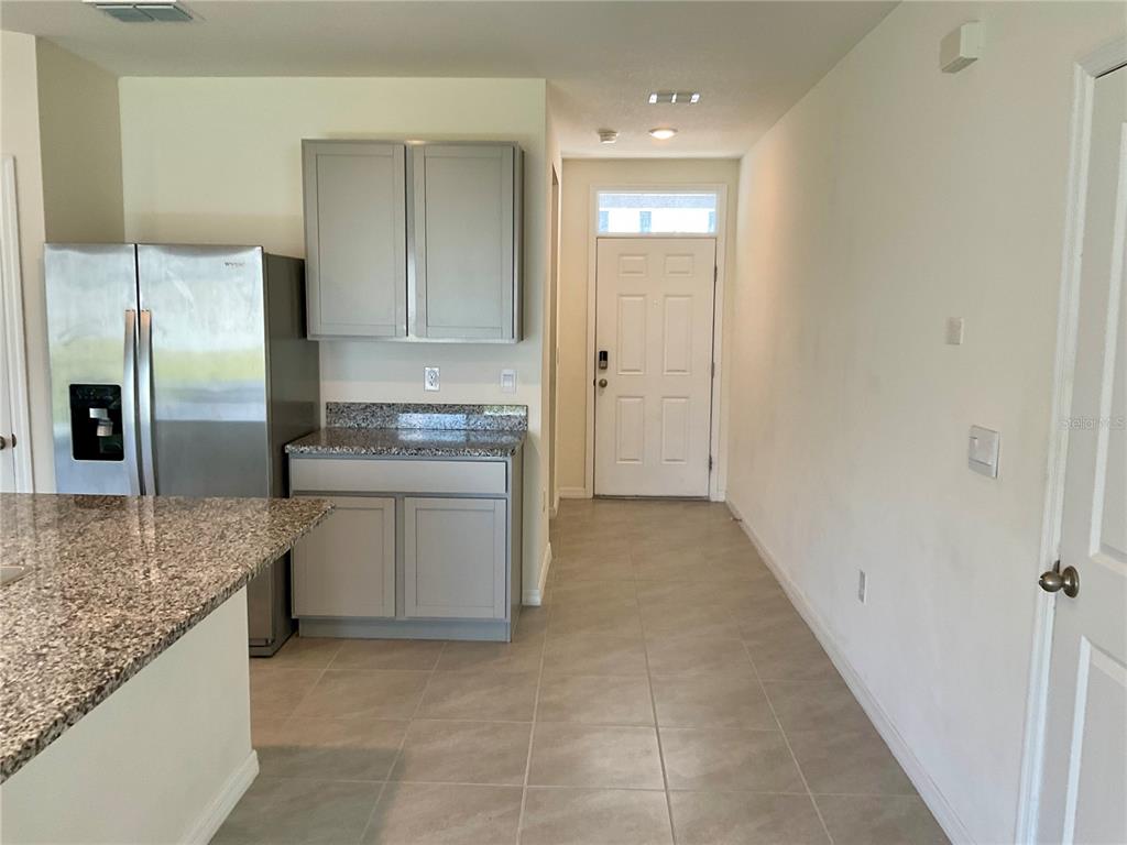 A kitchen area features gray cabinets, granite countertops, a stainless steel refrigerator, and tiled flooring — 33409 FIELD MAPLE LOOP, WESLEY CHAPEL, FL