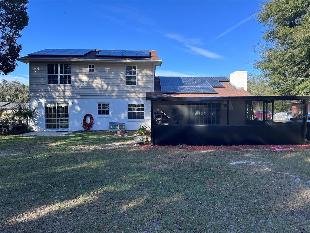 The rear exterior of a two-story house features solar panels, a screened-in porch, and siding — 5710 JACQULYN DRIVE, ZELLWOOD, FL