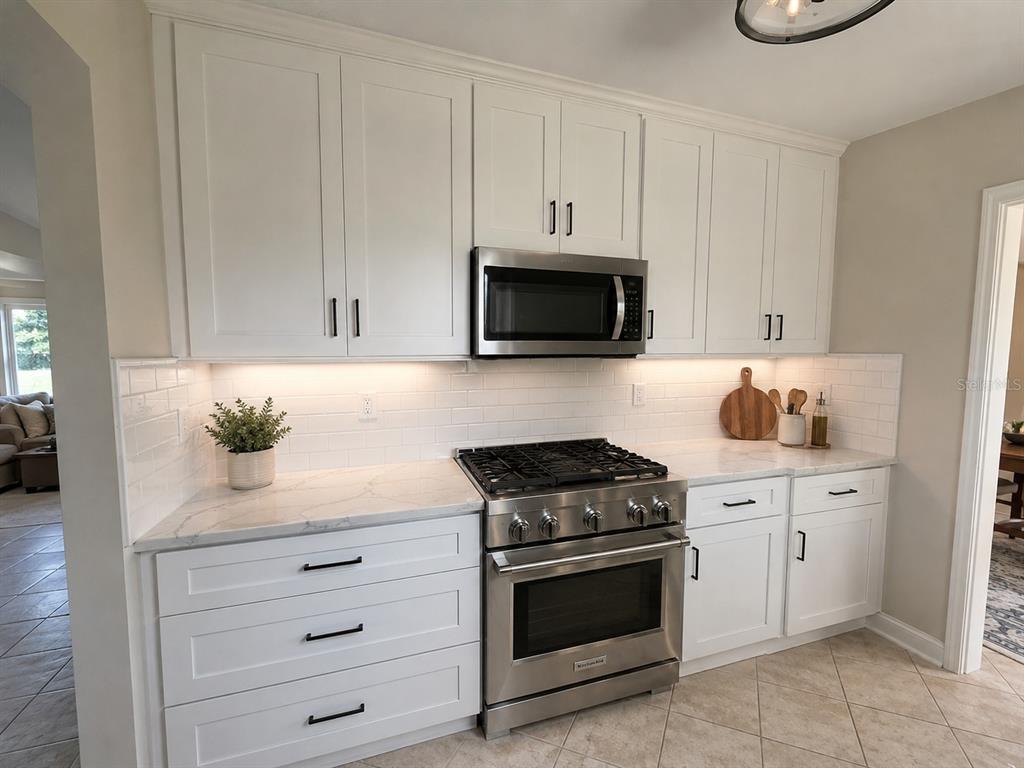 A kitchen features white shaker cabinets, stainless steel appliances, marble-look countertops, and a subway tile backsplash — 401 PATICA ROAD NE, ST PETERSBURG, FL