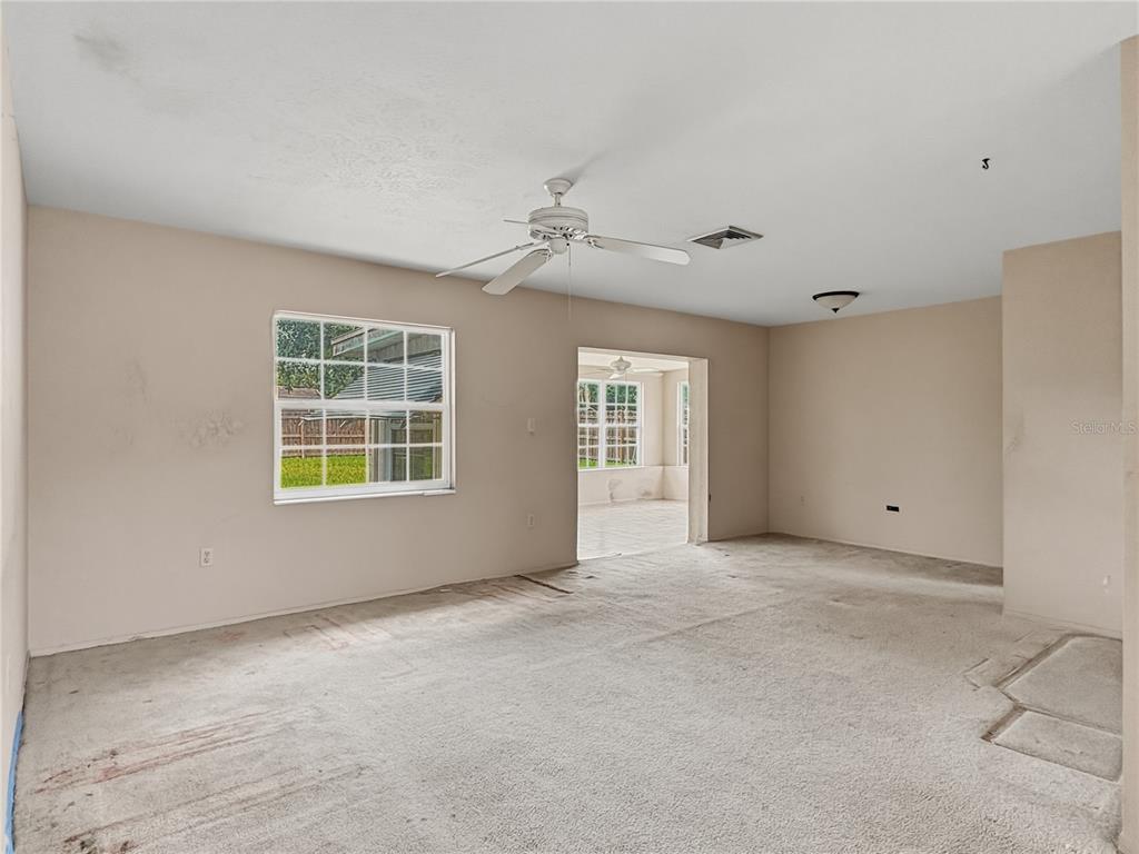 An empty living room with beige walls, carpeted flooring, a ceiling fan, and a window — 5430 HAYDEN BOULEVARD, SARASOTA, FL