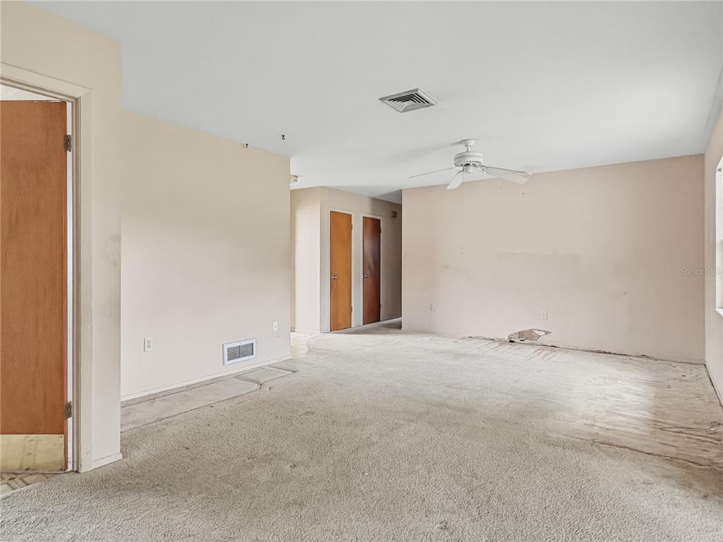 An empty room with beige walls, tan carpeting, a ceiling fan, and two wooden doors — 5430 HAYDEN BOULEVARD, SARASOTA, FL