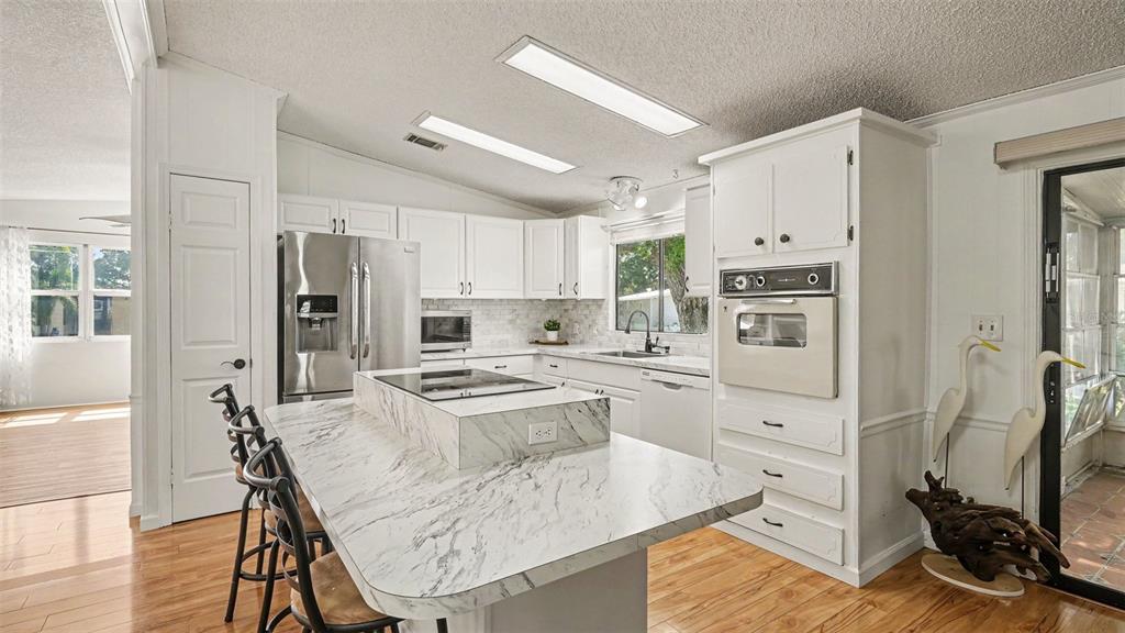A kitchen features white cabinets, a marble-topped island with a cooktop, and stainless steel appliances — 8430 IMPERIAL CIRCLE, PALMETTO, FL