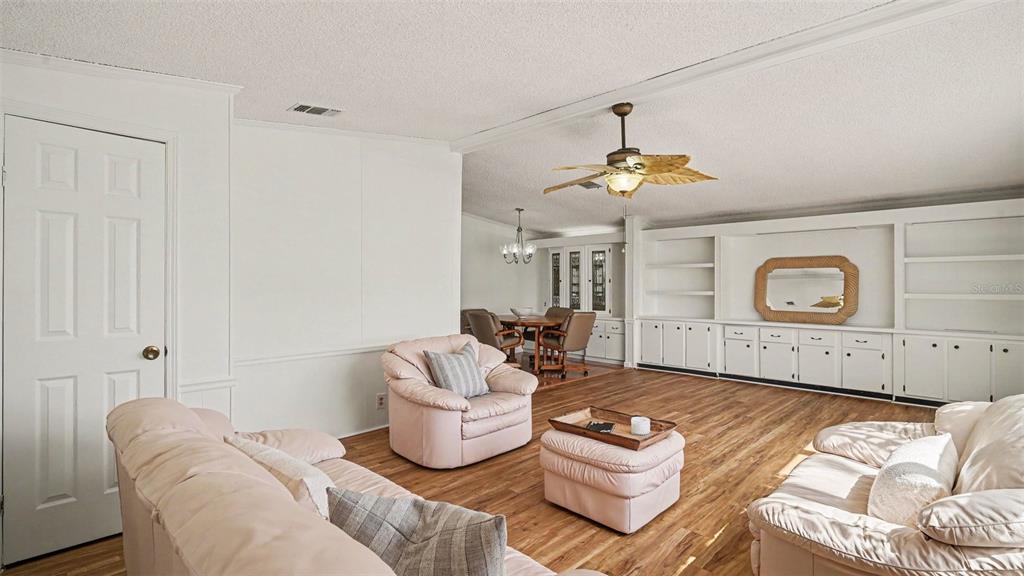 A living room with light-colored furniture, wood-look flooring, and built-in shelving along the wall — 8430 IMPERIAL CIRCLE, PALMETTO, FL