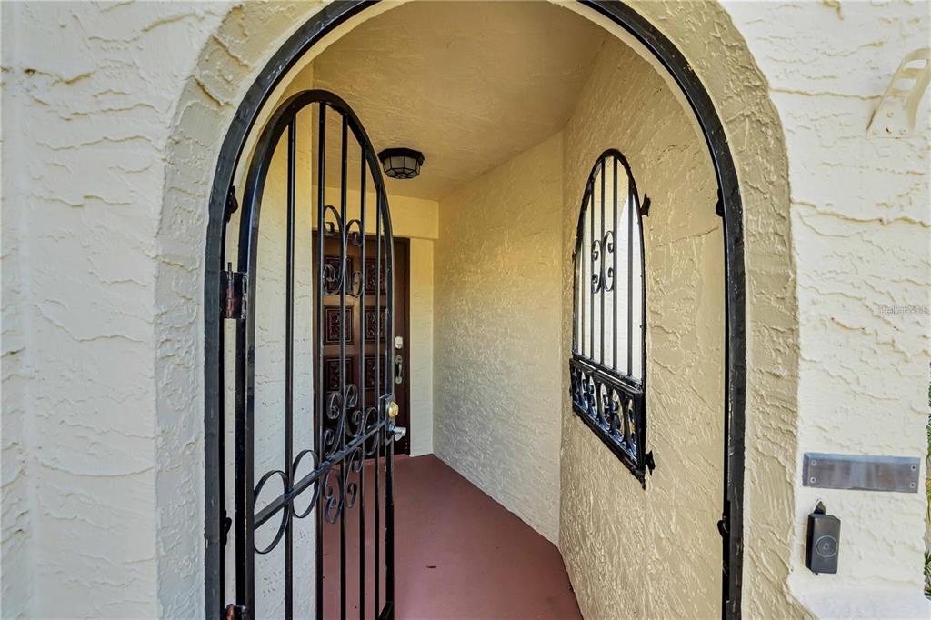 An arched entryway features a black metal gate, a textured wall, and a wooden door — 6101 34TH ST W UNIT 27C, BRADENTON, FL
